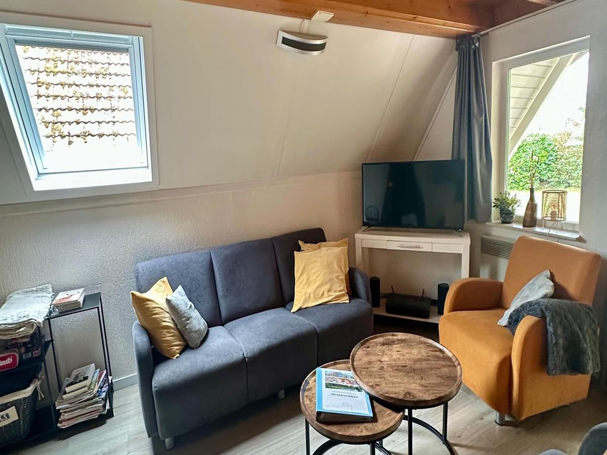 Ein modernes Wohnzimmer mit grauem Sofa, einem Holztisch, einem Fernseher auf einem weißen Schrank und einem Fenster mit Vorhängen.