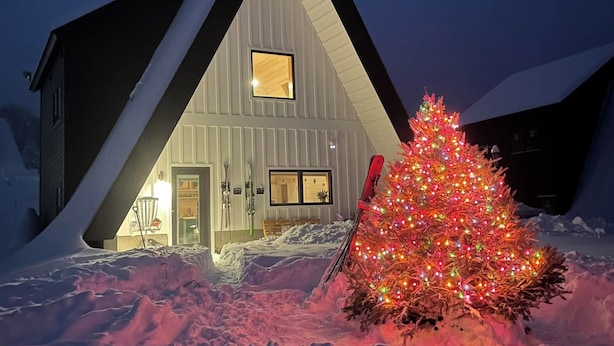 Een huis bedekt met sneeuw, met een verlichte kerstboom ervoor.