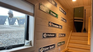 Een houten interieur met een raam dat uitkijkt op een rotsachtig landschap, een trap en borden aan de muur met de namen van kamers.