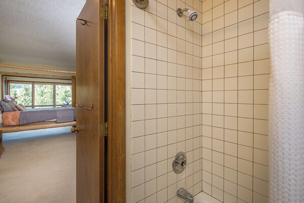 A bathroom with a shower, a toilet, and a sink. There is a window with a view of trees.