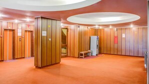 A hotel lobby with wooden panel walls, a central elevator, and a small seating area.