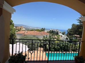 A balcony with a view of a swimming pool, a clear sky, and distant buildings.