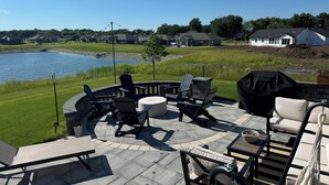 A patio with outdoor furniture, a grill, and a view of a lake and houses in the background. - Full home available for EAA 2025. Minimum 7 day rental. (Oshkosh)