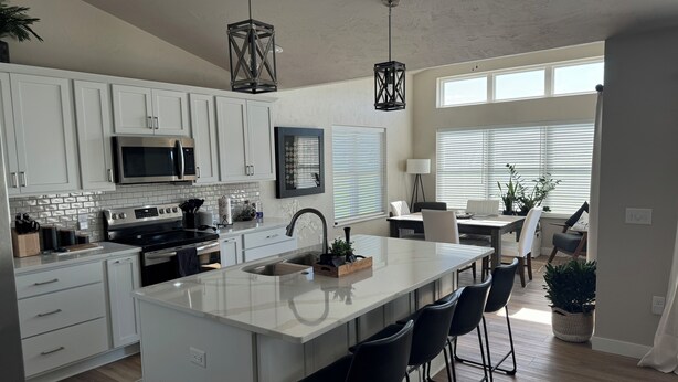 A modern kitchen with white cabinetry, a large island with bar stools, a microwave, and a hanging pendant light. - Full home available for EAA 2025. Minimum 7 day rental. (Oshkosh)