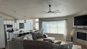 A modern living room with a sofa, a coffee table, and a fireplace. There is a kitchen area with white cabinets and a microwave. - Full home available for EAA 2025. Minimum 7 day rental. (Oshkosh)