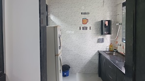 Cocina compacta con refrigerador, pileta y microondas. Hay letreros decorativos en la pared y un ventilador de techo.
