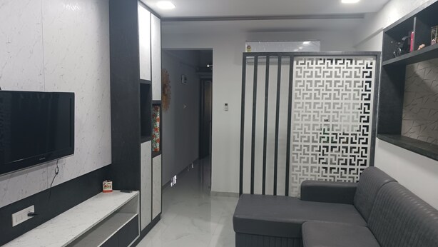 Una sala de estar moderna con un televisor de pantalla plana, un sofá gris y un separador decorativo con un diseño geométrico.