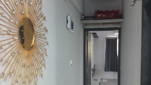 Un pasillo con un cuadro decorativo de diseño solar, una puerta blanca y un objeto rojo en el techo.