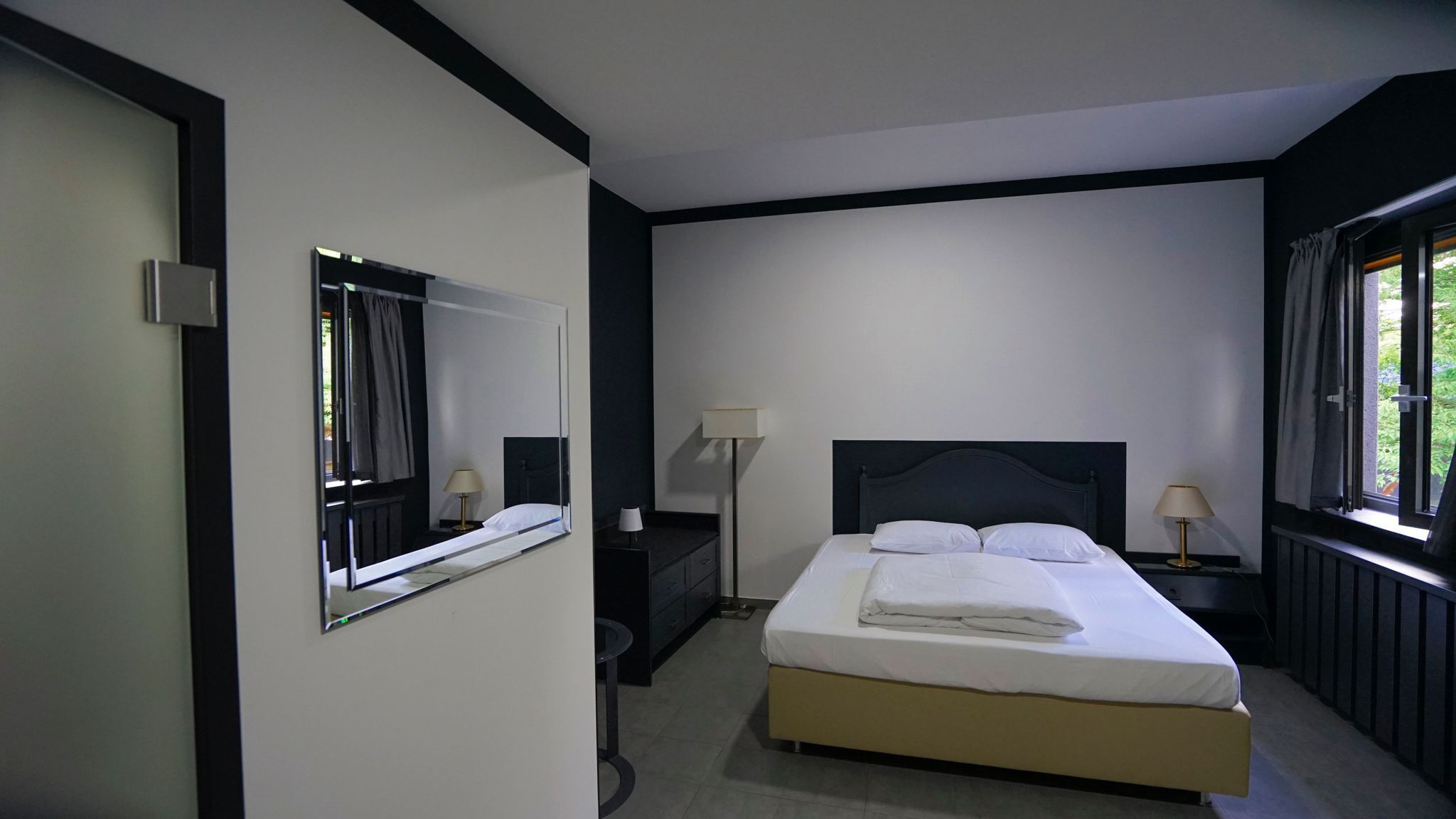 Un dormitorio con cama, lámparas de noche, un espejo y una ventana.