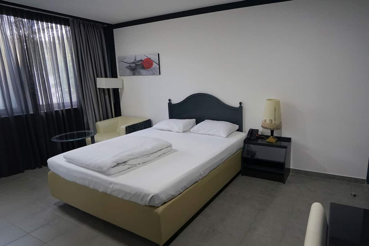 Een hotelkamer met een bed, nachtkastjes, een stoel, een bureau en een raam met gordijnen.