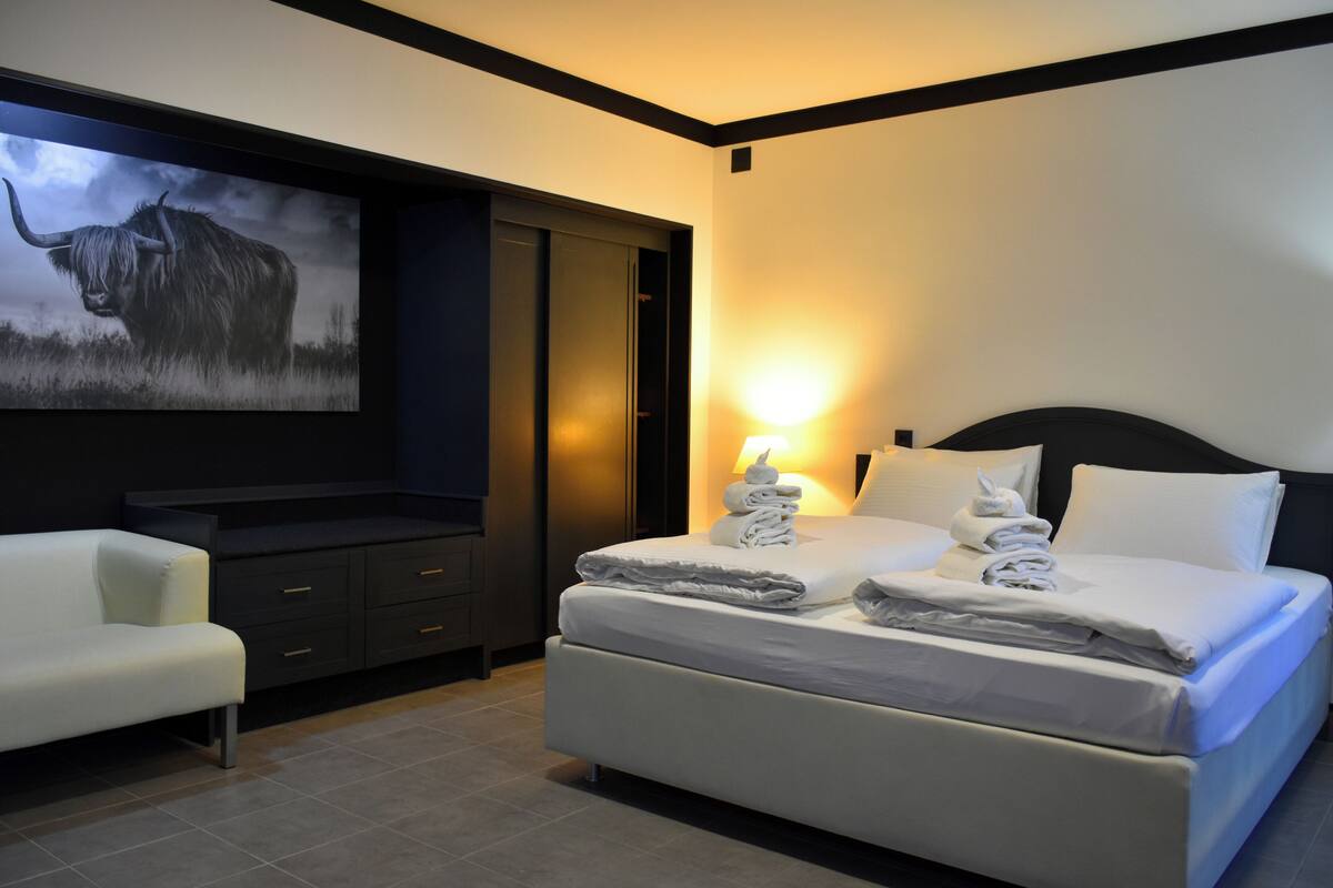 Een moderne hotelkamer met een groot bed, een zithoek en een aan de wand bevestigde televisie waarop een eland te zien is.