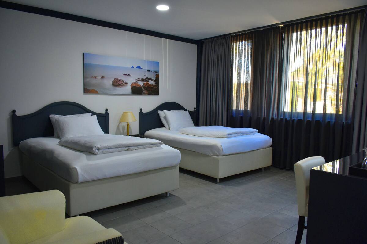 Een hotelkamer met twee bedden, een bureau, een stoel, een lamp en een schilderij aan de muur.