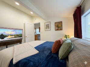 Un dormitorio con cama, televisor, puerta y ventana con cortinas.