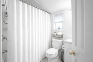 Ein Badezimmer mit Duschvorhang, Toilette und Fenster über der Toilette.