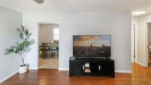 Un salon avec un tableau représentant un paysage urbain, un meuble de rangement noir pour appareils électroniques et une plante en pot.