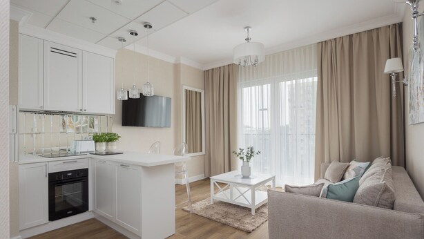 A modern kitchen with white cabinetry, a built-in oven, and a dining area with a white table and chairs.