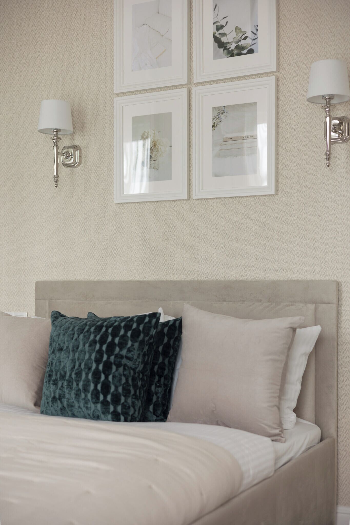 A bedroom with a bed, two wall-mounted lamps, and four framed pictures on the wall.