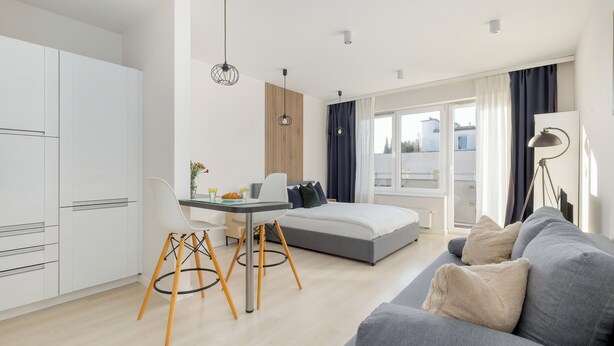 A modern hotel room with a bed, a gray sofa, a dining area with a table and chairs, and a kitchenette. - Potulicka Coffee Studio (Szczecin)