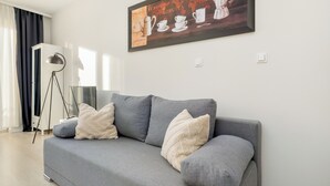 A modern living room with a grey sofa, two white throw pillows, a floor lamp, and a framed coffee-themed artwork on the wall. - Potulicka Coffee Studio (Szczecin)