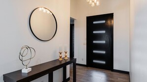 Un pasillo con una consola de madera oscura, un espejo redondo y una puerta negra con paneles iluminados.