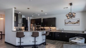 Una cocina moderna con armarios oscuros, una isla central con taburetes de bar, electrodomésticos de acero inoxidable e iluminación colgante.