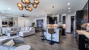 Una cocina moderna con armarios oscuros, una isla central con taburetes de bar y un comedor con sofá y mesa de centro.