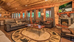 A cozy cabin interior with a fireplace, leather sofas, a coffee table, and a large rug with animal prints. - Cliffside Mountain View - Private indoor pool, gorgeous views, theater, game room, and more! (Sevierville)