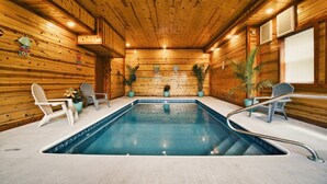 A wooden cabin with a pool, Adirondack chairs, and potted plants. - Cliffside Mountain View - Private indoor pool, gorgeous views, theater, game room, and more! (Sevierville)