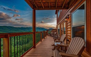Eine Holzterrasse mit Stühlen und einer Glastür, mit Blick auf eine gebirgige Landschaft.
