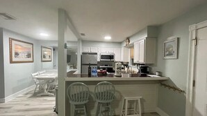 Une cuisine moderne avec des meubles blancs, un îlot central doté de tabourets et un coin repas avec une table et des chaises.