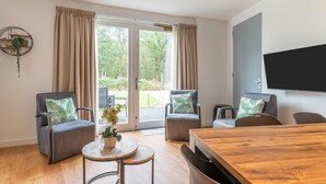 A modern living room with two grey armchairs, a wooden coffee table, and a large TV mounted on the wall. - holiday home in Goirle with sauna (Goirle)