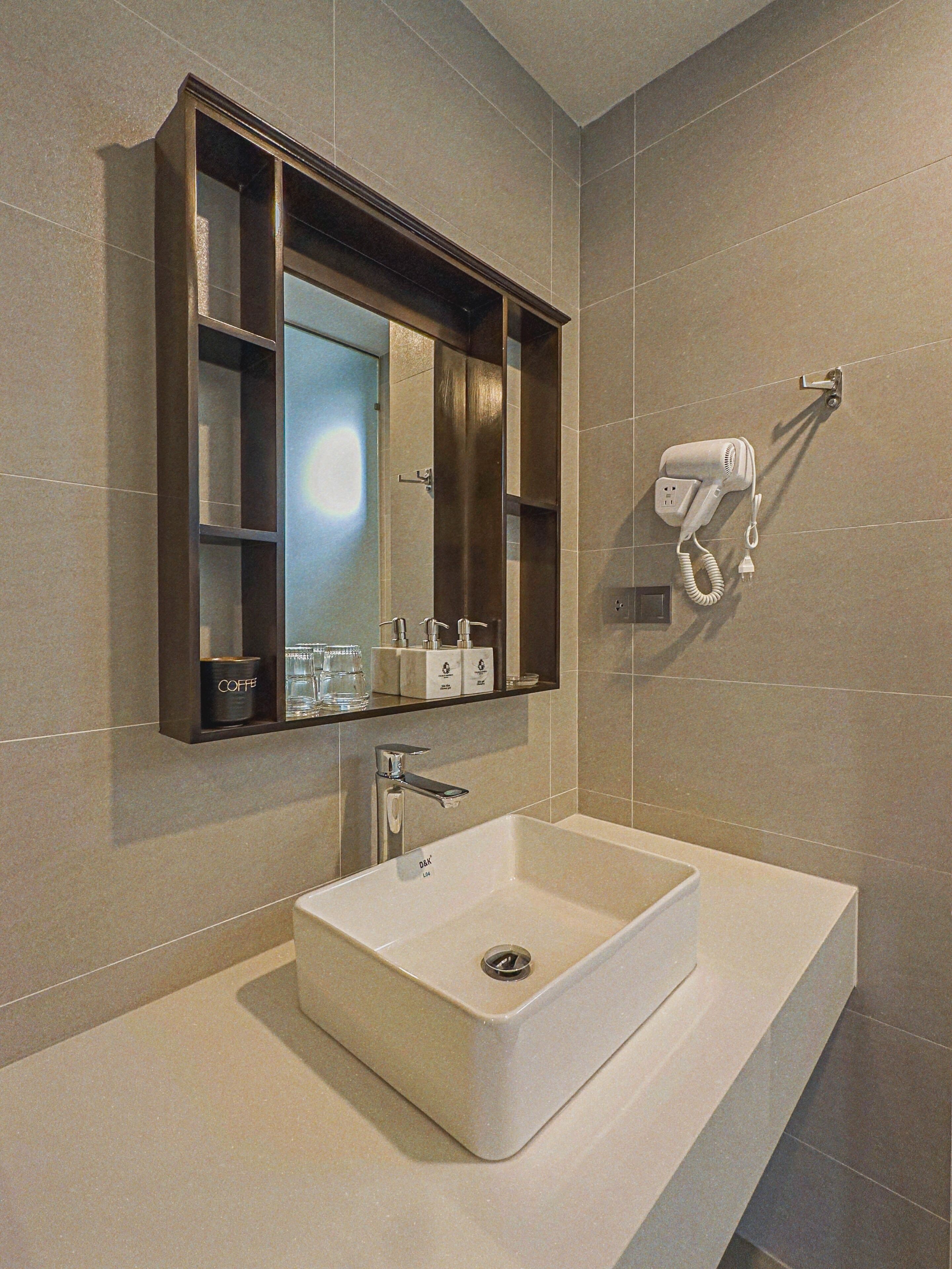A modern bathroom with a large rectangular sink, a mirror with a dark frame, and a hairdryer mounted on the wall.