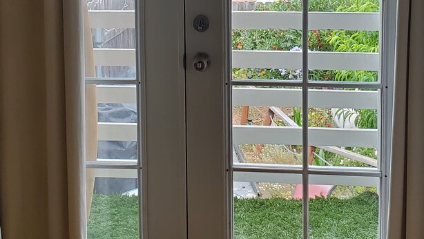 A sliding glass door leading to a balcony with a view of a garden and distant hills.