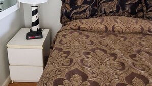 A bedroom with a patterned bedspread, a bedside lamp, a digital clock, and a framed picture on the wall.
