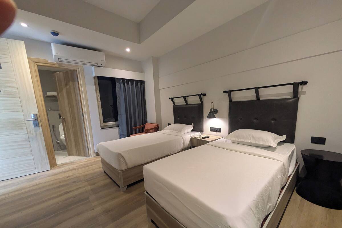 Una habitación de hotel moderna con dos camas, un escritorio pequeño, una silla y una ventana con cortinas.