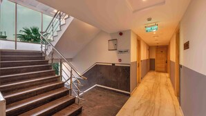 Interior moderno de hotel com escada, sinal de saída de incêndio e corredor que leva a uma porta.