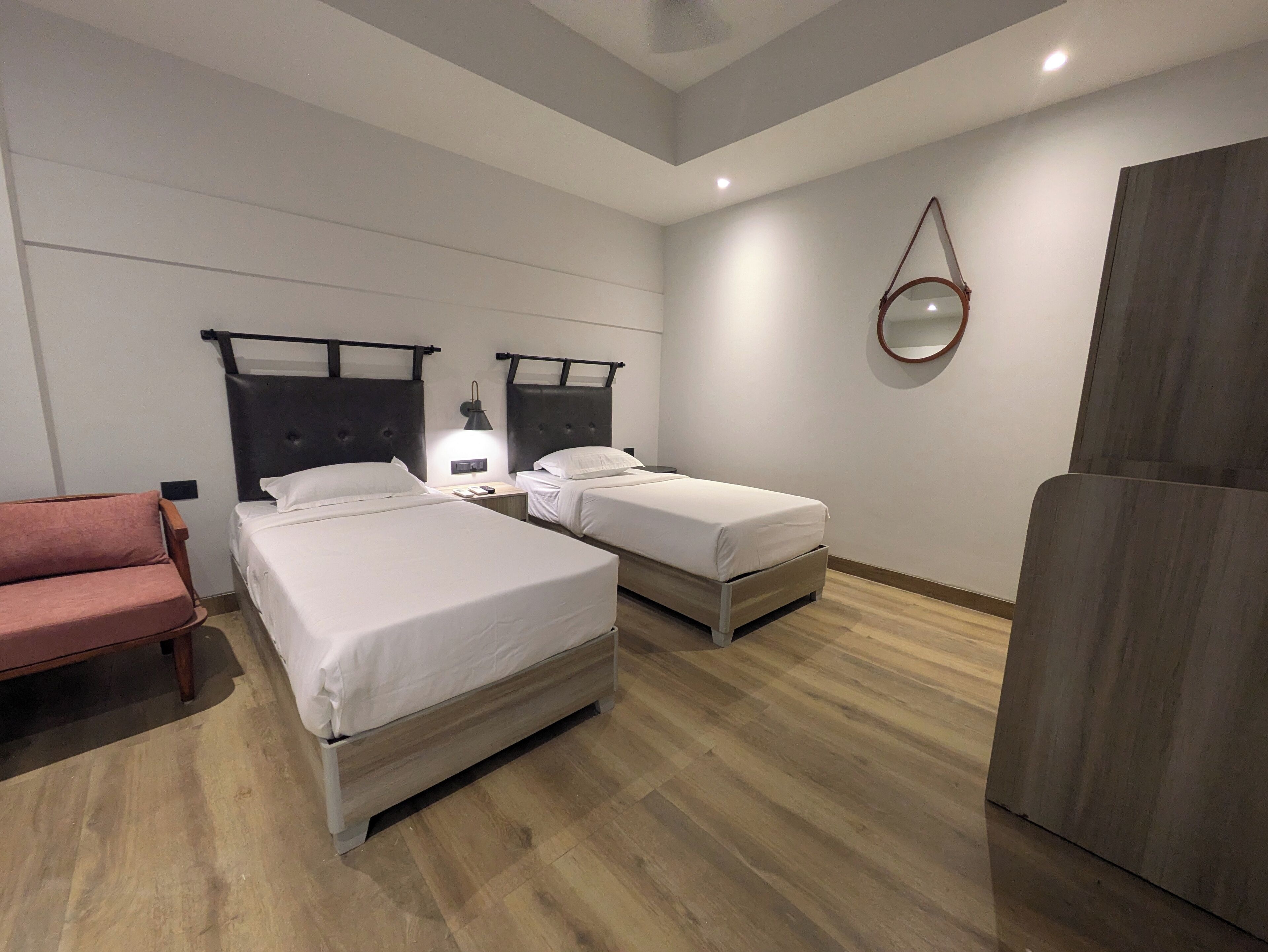 A hotel room with two single beds, a wooden floor, a small seating area, and a mirror on the wall.