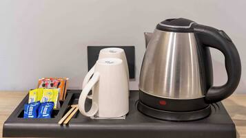 A kitchen counter with a stainless steel kettle, a white mug, and a tea set.