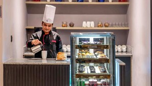 Um chef servindo uma bebida em um balcão com uma vitrine de doces e uma seção refrigerada.
