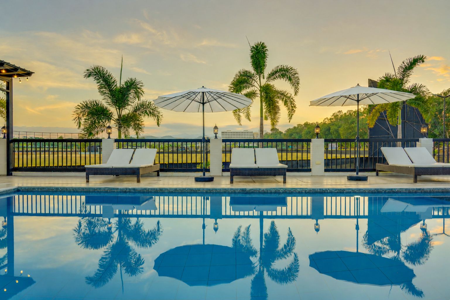 Zona de piscina con sillas de descanso y sombrillas, rodeada de palmeras y vistas al paisaje.