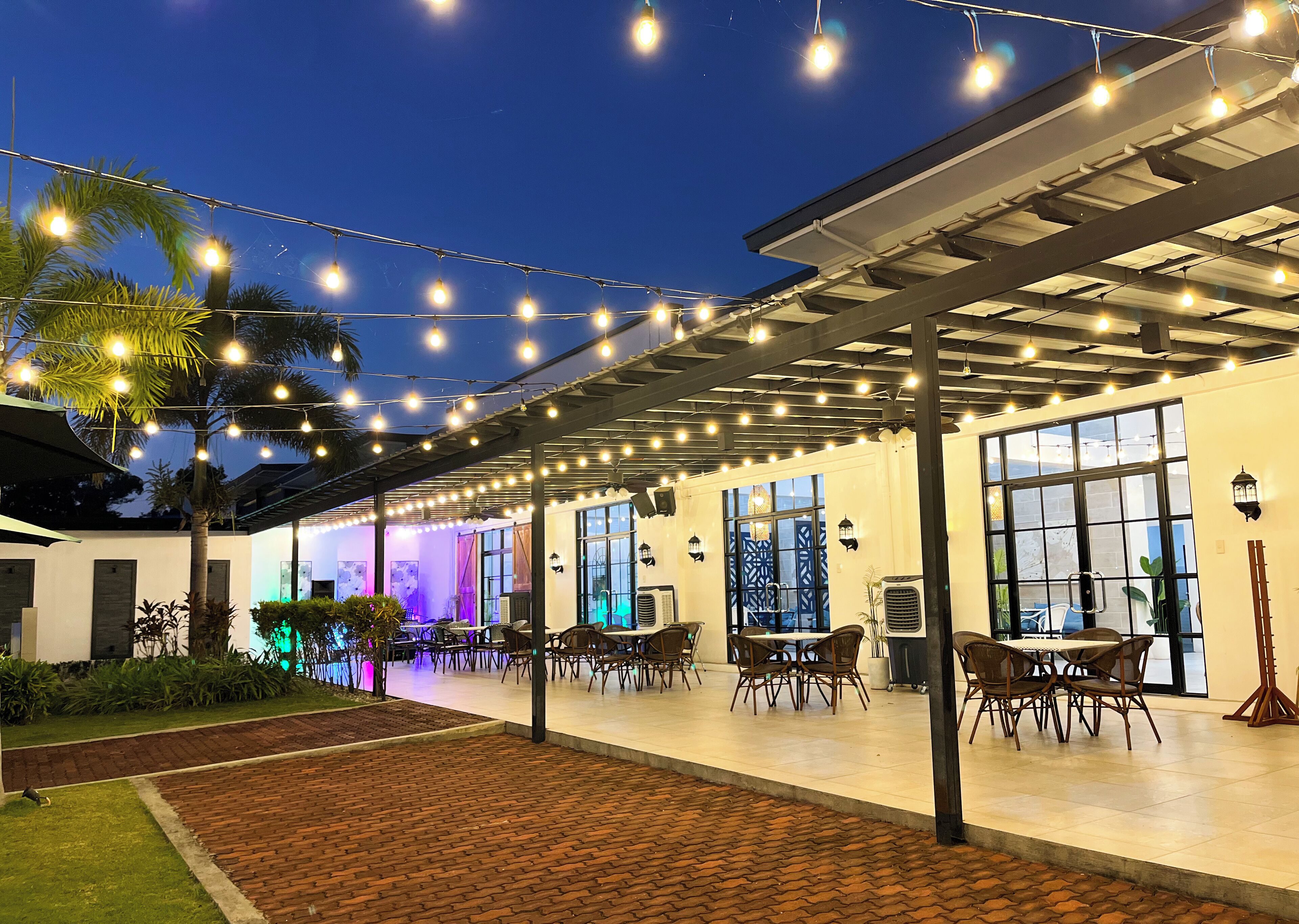 An outdoor patio area with string lights, tables, chairs, and a brick pathway.