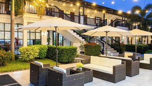 Een terras met rieten meubels en parasols, een trap en lichtslingers.