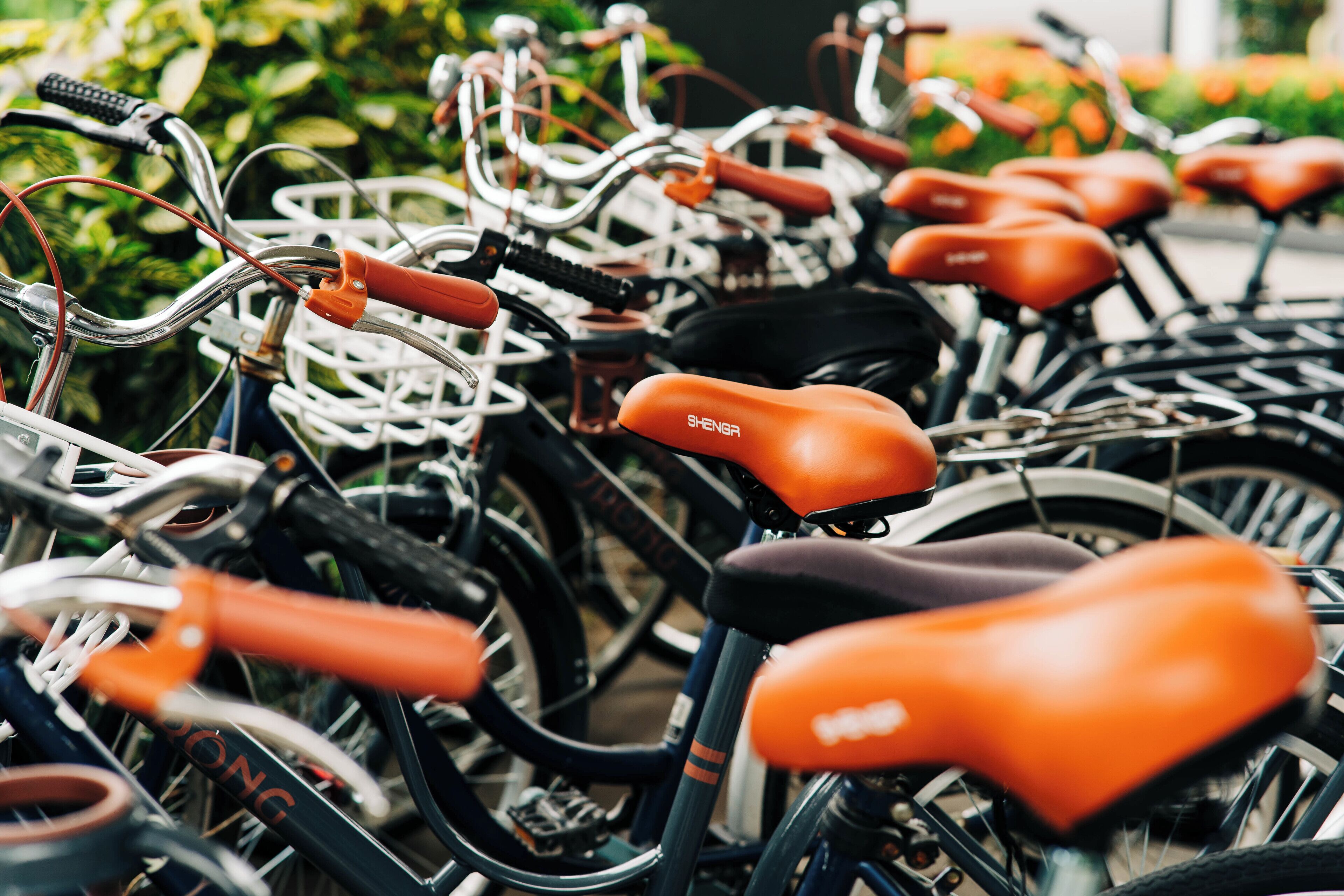 Une rangée de vélos avec des selles orange et des guidons noirs, garés très près les uns des autres.
