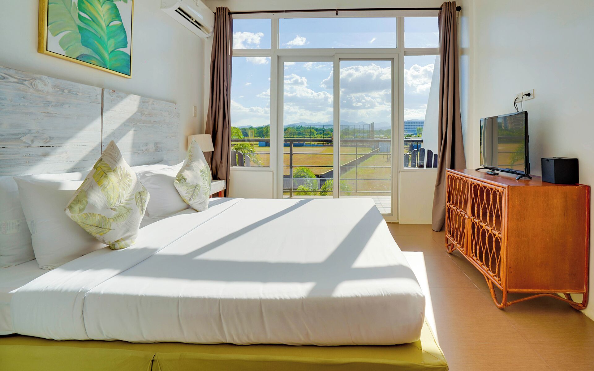 A hotel room with a large bed, a television, and a view of the outdoors.