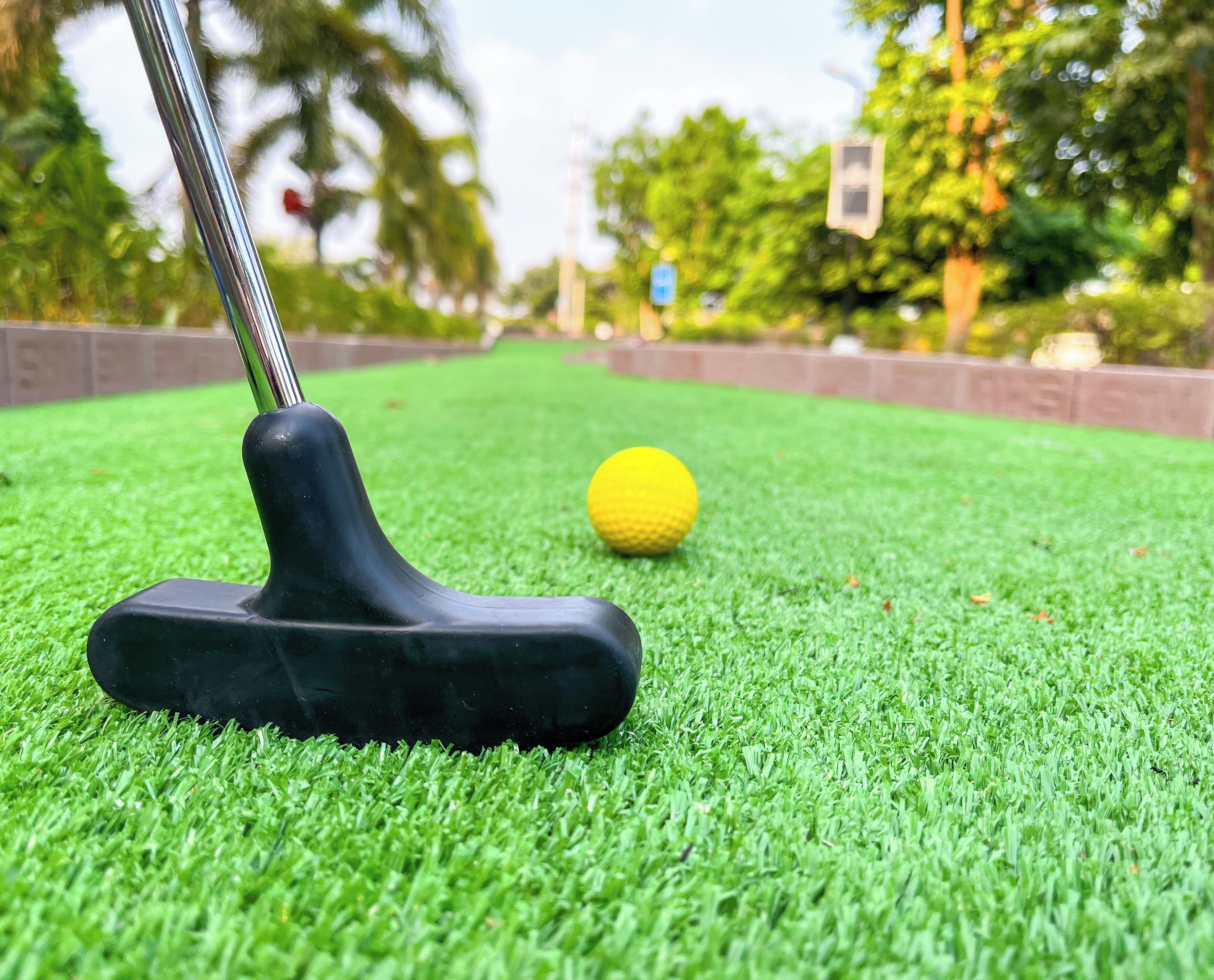 A golf club on artificial grass with a golf ball in the background.