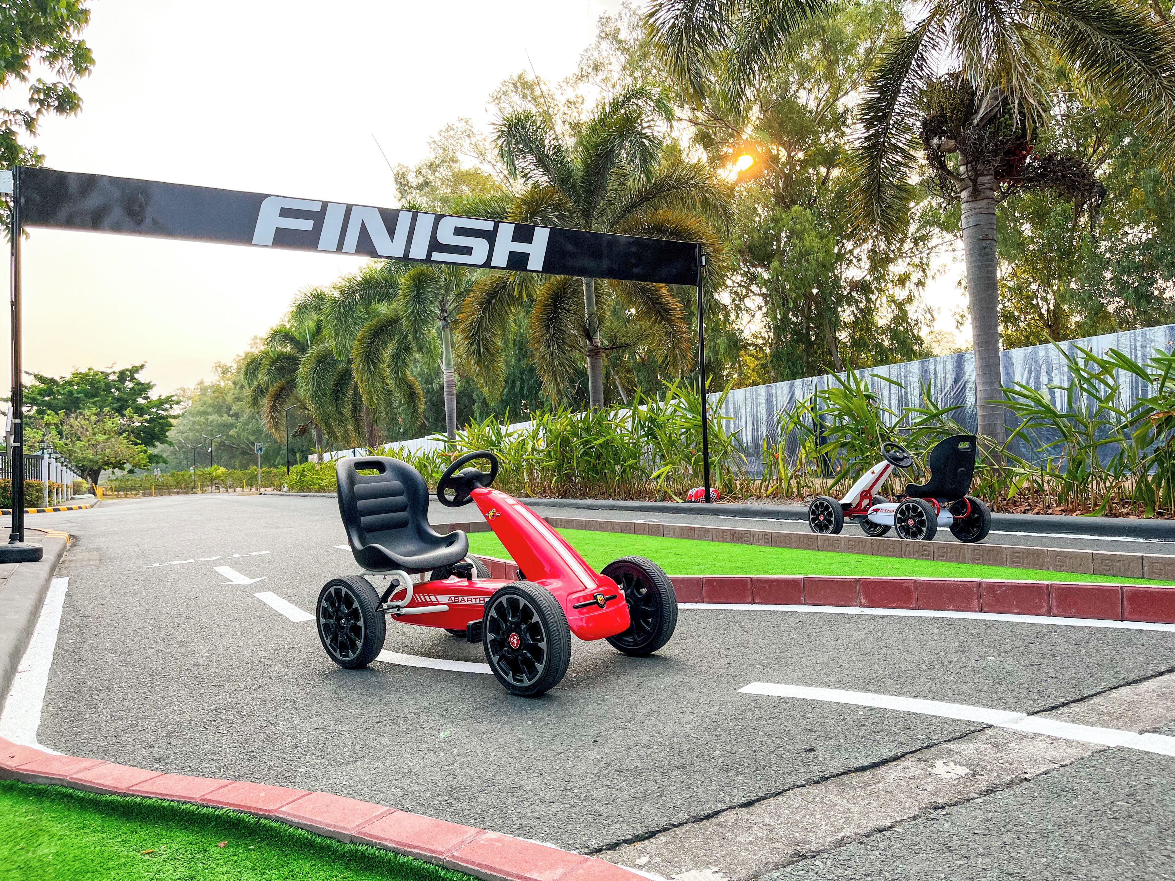 Pista de kart com arco de linha de chegada, vegetação e estrada pavimentada.