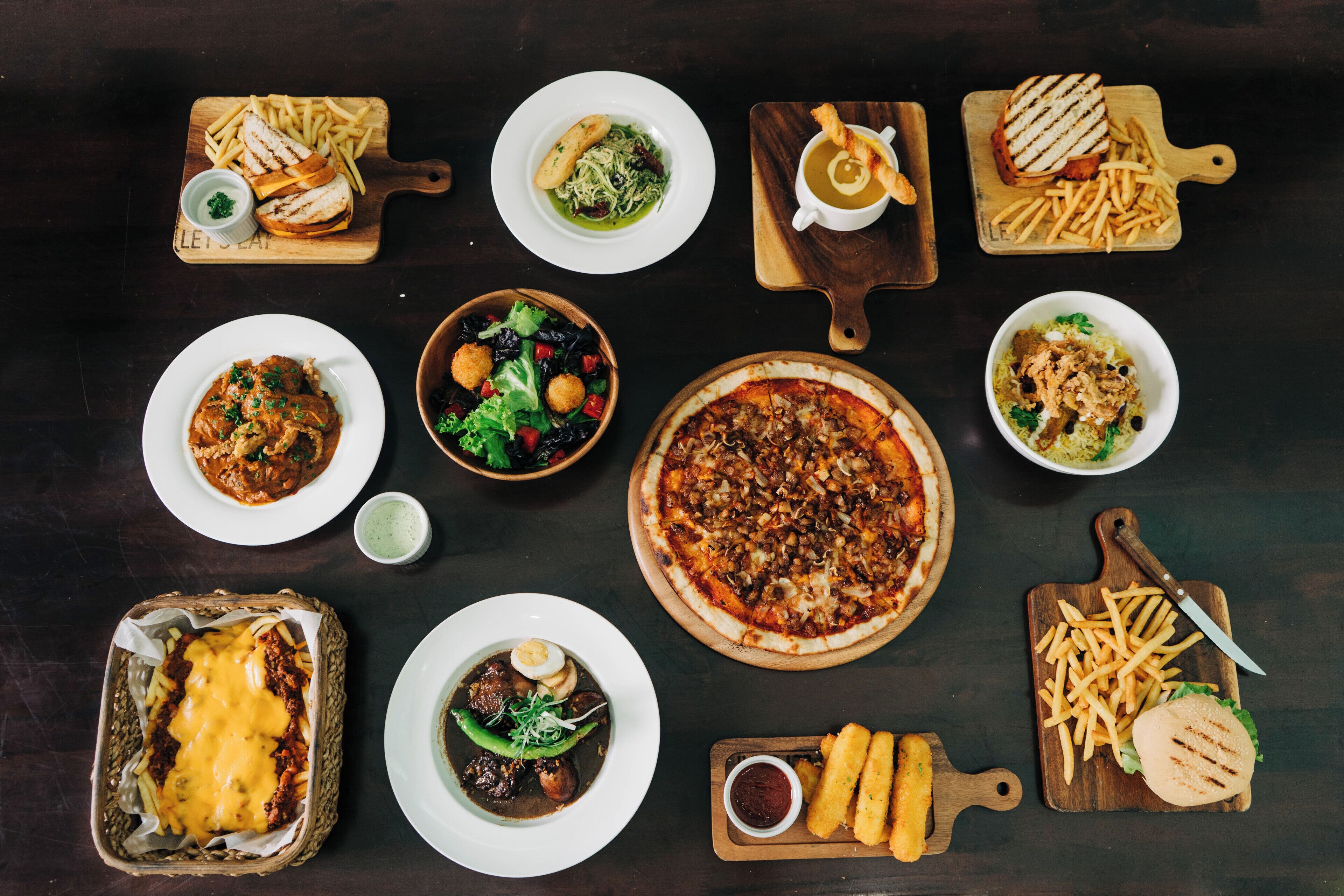 A variety of dishes including a pizza, pasta, and salads, arranged on a dark table.