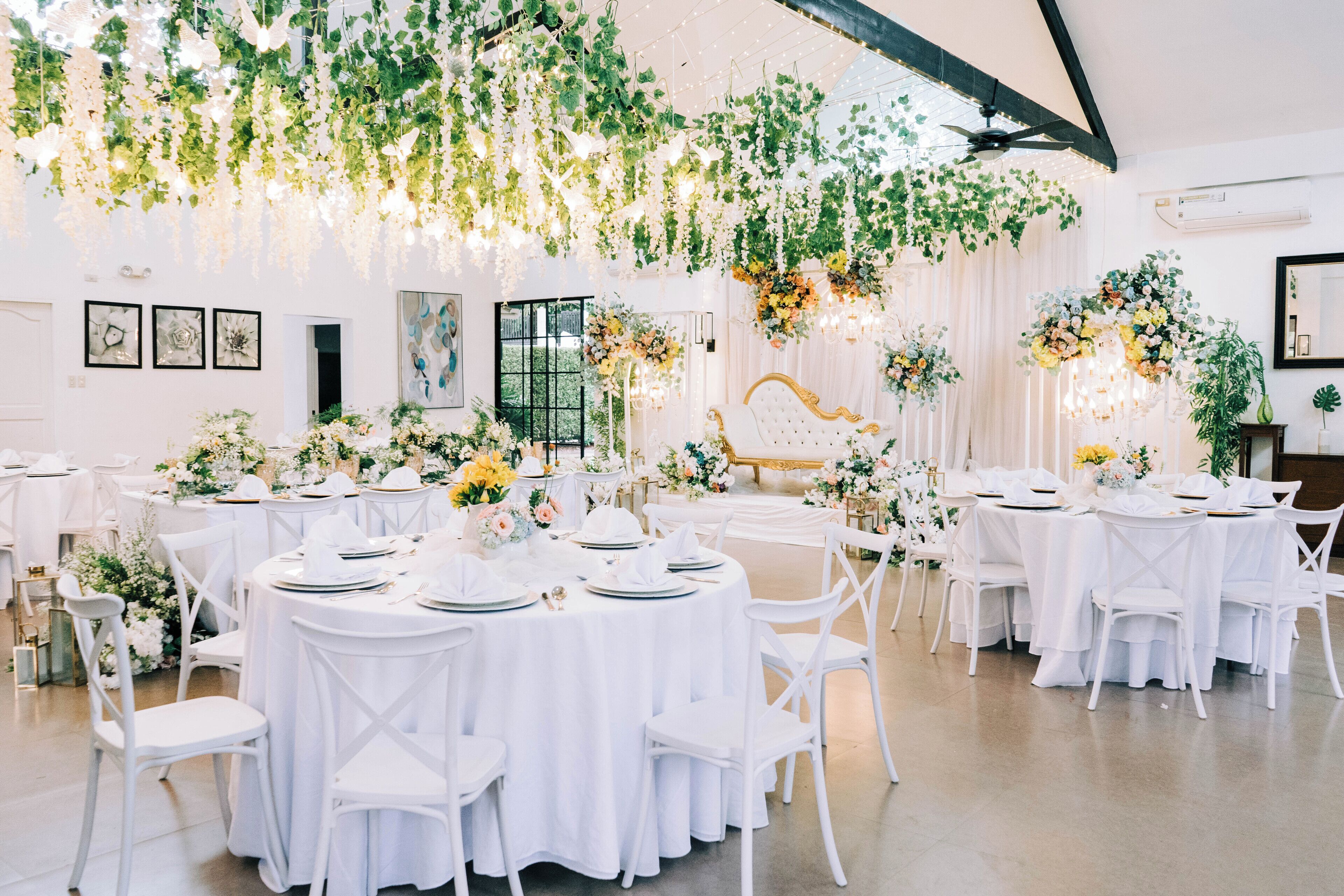 Een balzaal met ronde tafels, bedekt met witte tafelkleden, witte stoelen en bloemdecoraties.