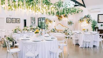 Een balzaal met ronde tafels, bedekt met witte tafelkleden, witte stoelen en bloemdecoraties.