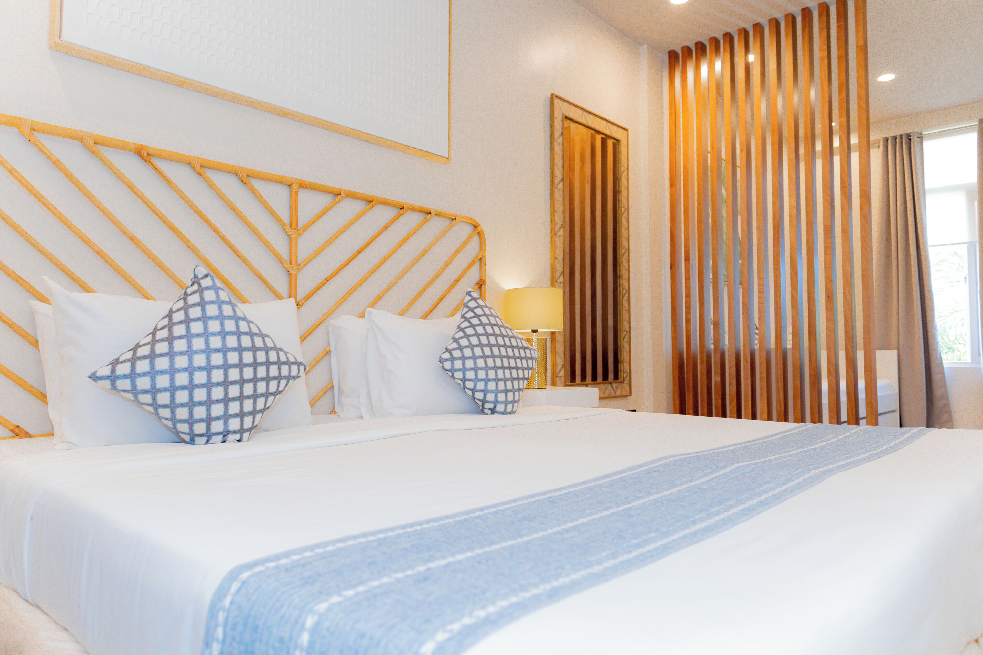 Une chambre d’hôtel avec un lit, des oreillers, une table de chevet, une lampe et une fenêtre avec des rideaux.